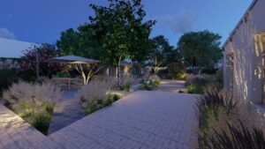 Jardin nocturne éclairé avec terrasse pavée, coin repas sous parasol, et végétation luxuriante, ambiance sereine.