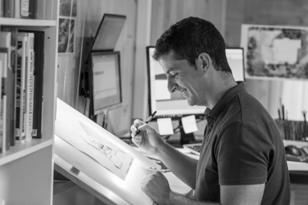 Architecte au travail : Design et dessin de plans. Architecte souriant traçant un plan détaillé sur une table lumineuse. Il travaille dans son bureau, près d'une bibliothèque.