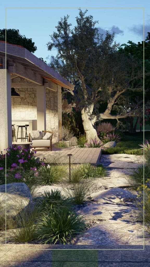 Patio rustique avec murs de pierre et mobilier extérieur. Éclairage chaud sur un grand olivier et un chemin de dalles de pierre dans le jardin.